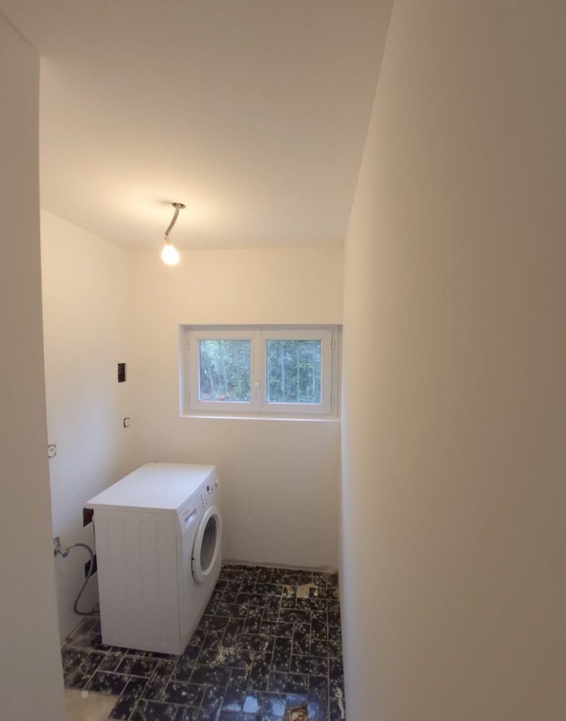 La même buanderie terminée : murs et plafond peints en blanc, finition nette autour de la fenêtre