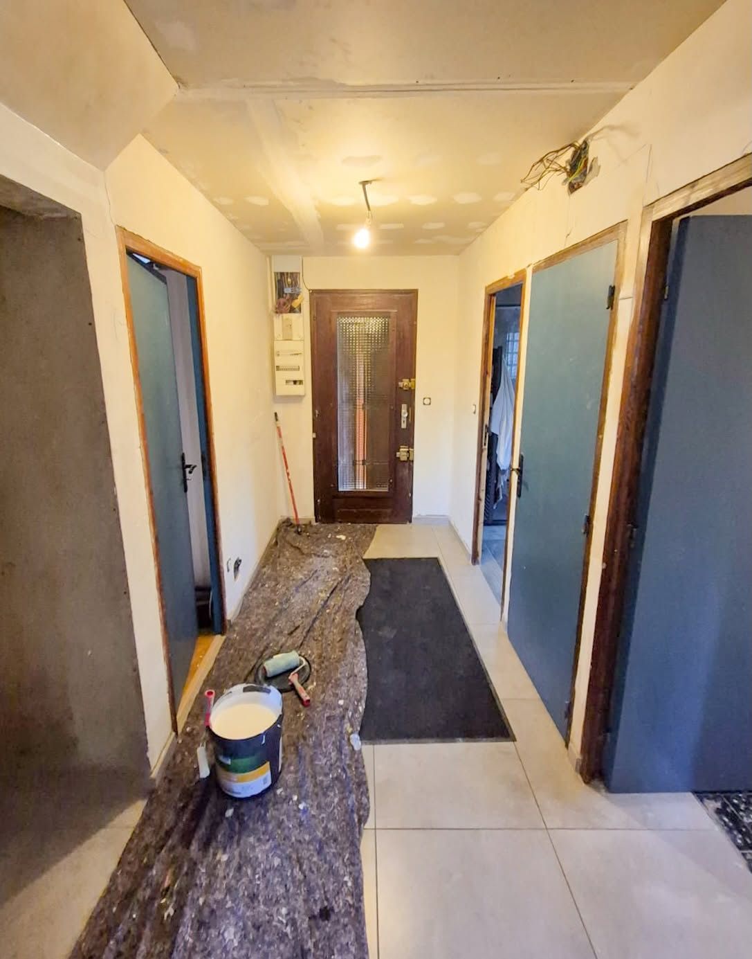 Couloir en cours de chantier : sol bâché, pot de peinture, murs et encadrements en cours de reprise