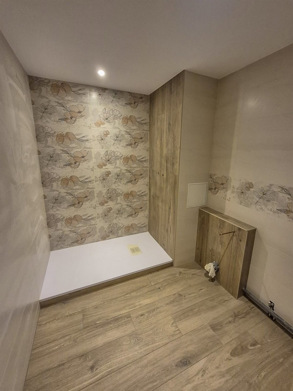 La même salle de bain terminée : douche carrelée à décor floral, habillage effet bois et sol effet parquet