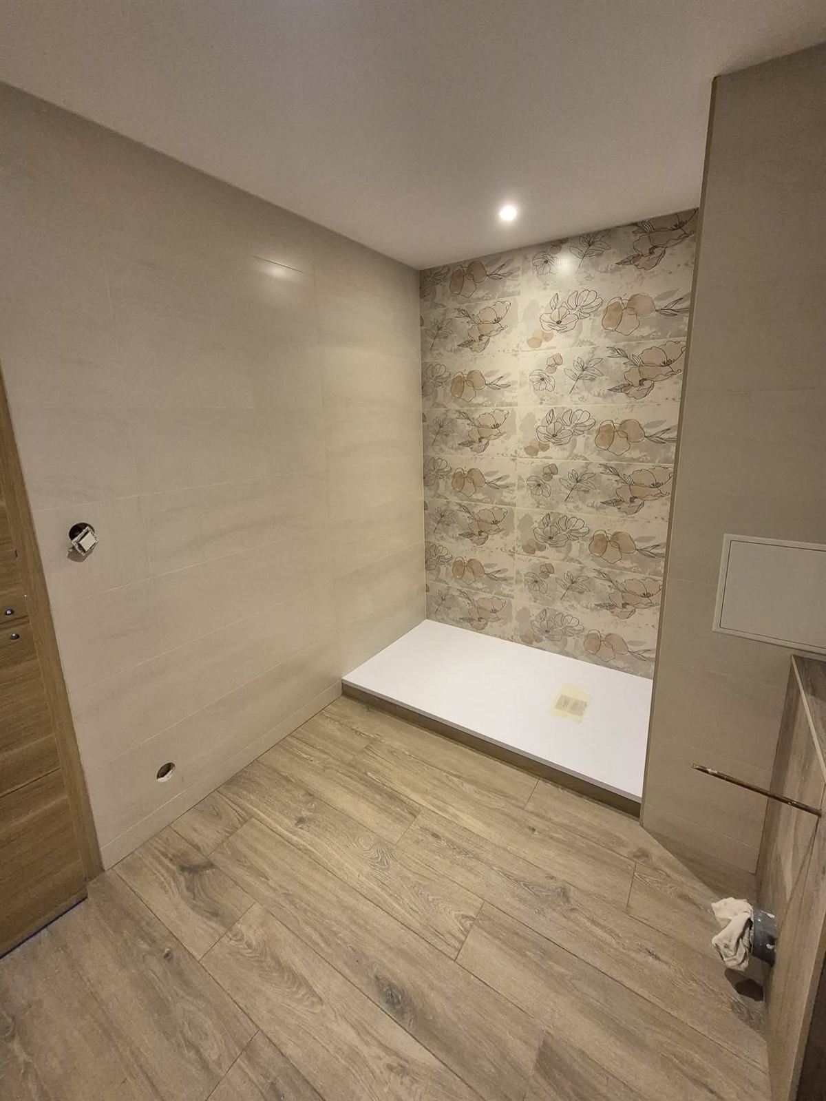La même salle d'eau terminée : murs clairs, pan de papier peint à motif, receveur de douche extra-plat et sol effet parquet