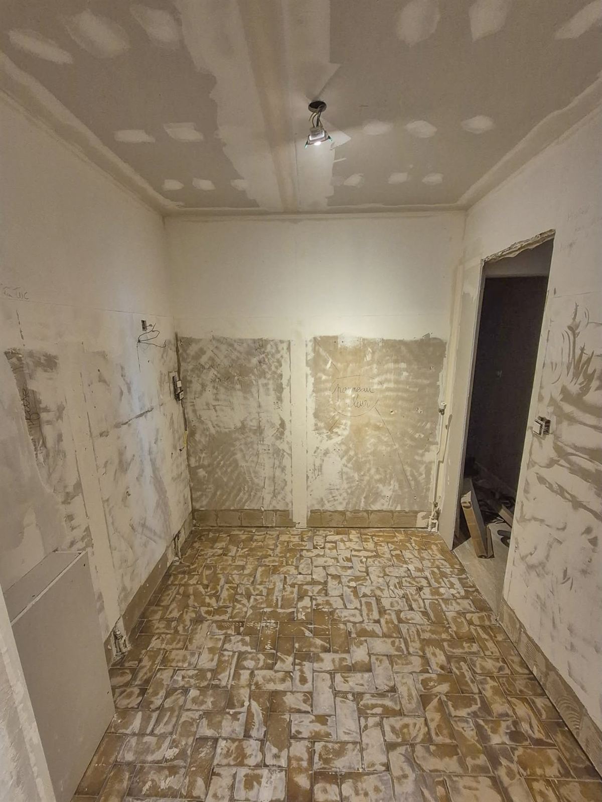 Salle d'eau avant travaux : murs décapés jusqu'au plâtre et ancien carrelage de sol en partie cassé