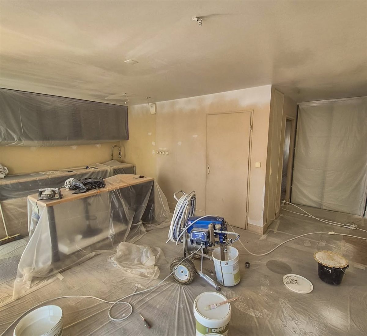 Séjour en cours de chantier : sols et mobilier protégés par des bâches, station de peinture airless en place