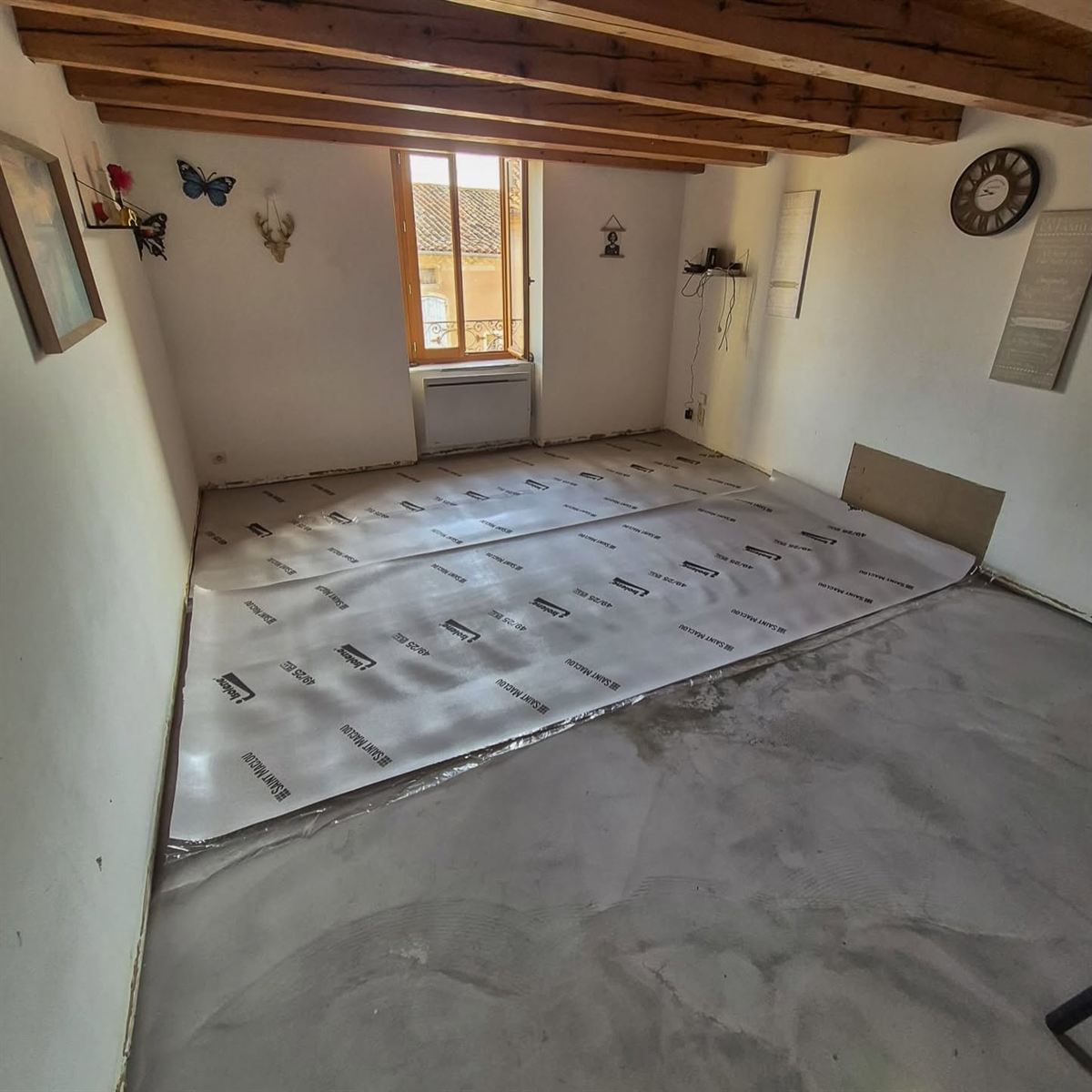 Séjour à poutres apparentes avant la pose du sol : dalle béton ragréée et sous-couche déroulée