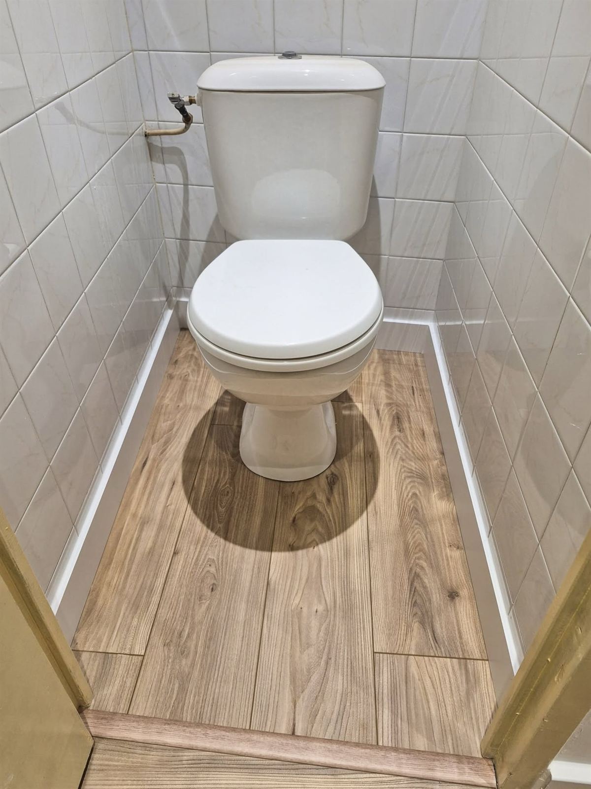 Le même WC terminé : faïence claire jusqu'au plafond et sol effet parquet