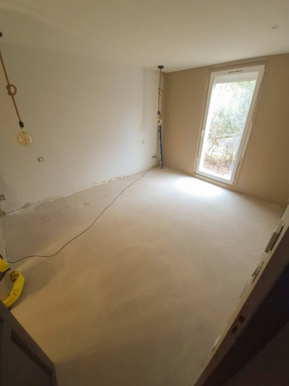 Angle d'une pièce revêtue d'un enduit décoratif clair, éclairé par une fenêtre haute