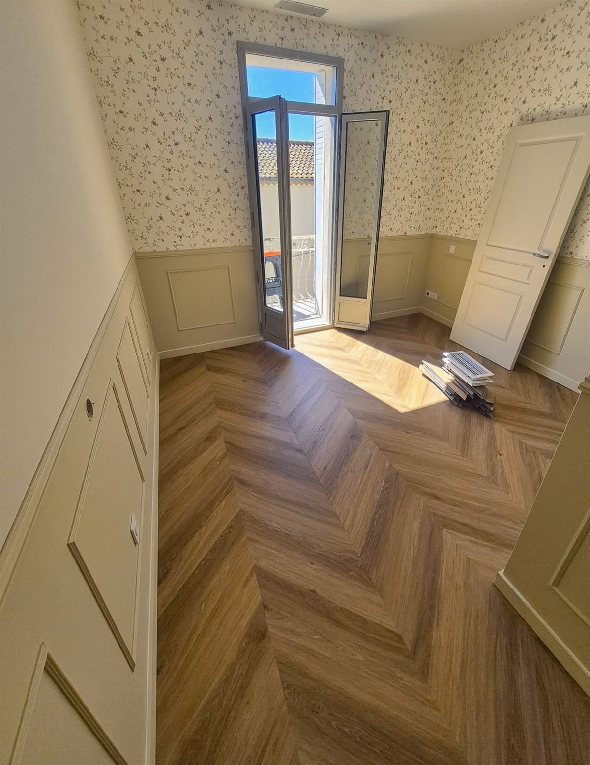 Chambre avec papier peint à petit motif clair au-dessus d'un soubassement mouluré peint, parquet à chevrons au sol