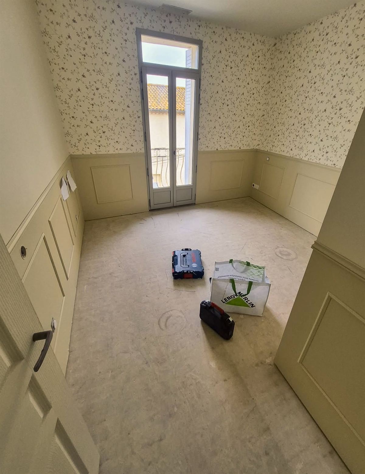 La même chambre vue depuis l'angle opposé : papier peint clair, soubassement mouluré et porte-fenêtre