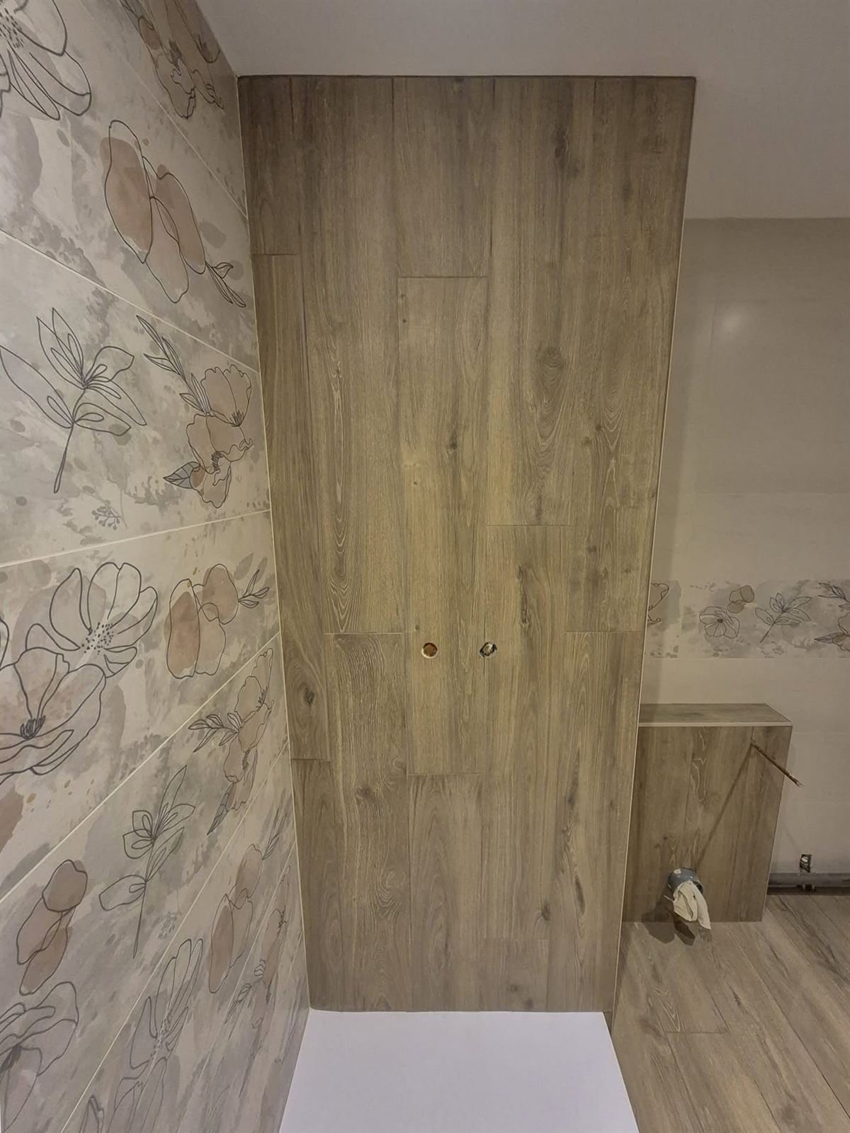 Détail d'un papier peint à grand motif floral encadrant un placard à portes en bois dans une salle d'eau