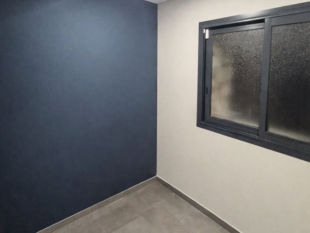 Angle de pièce peint en bleu nuit mat, contrastant avec le mur clair et la menuiserie aluminium noire