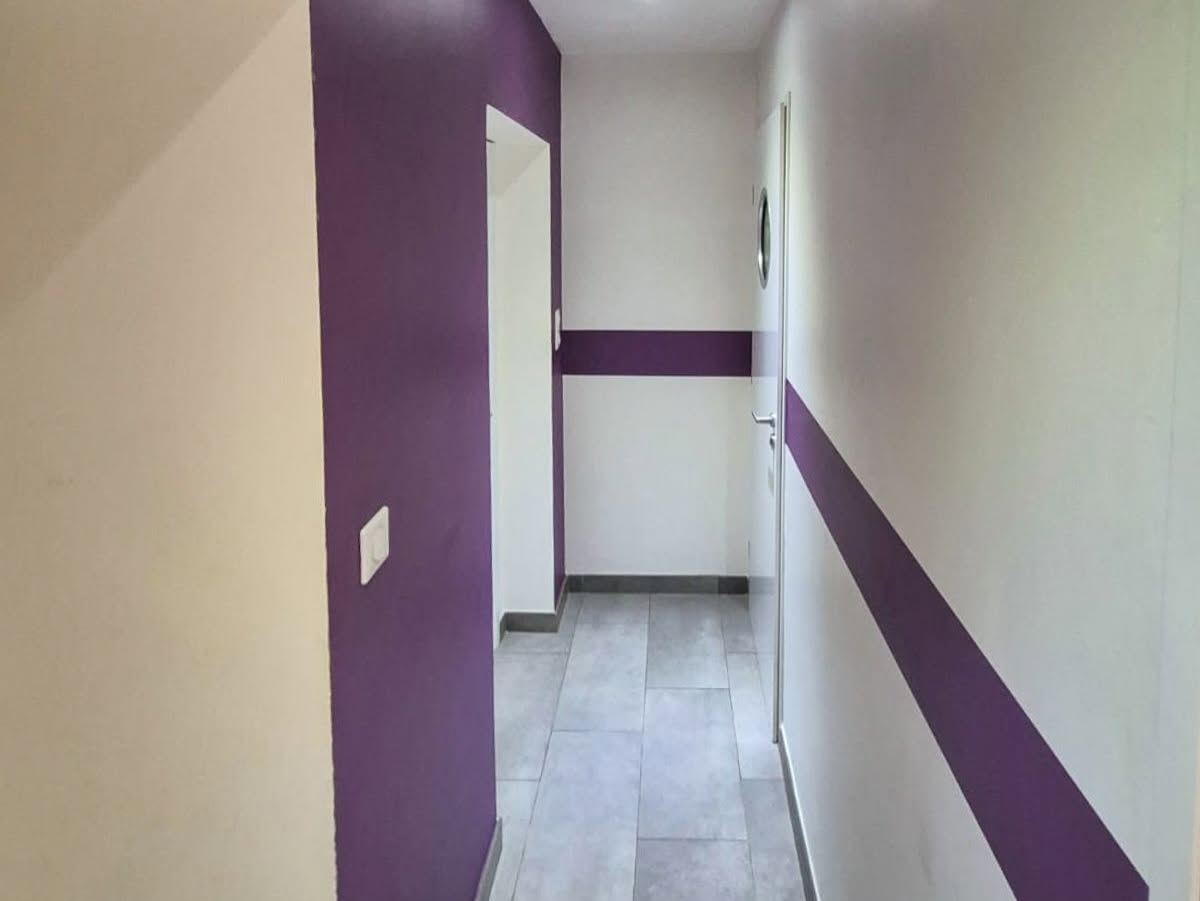 Couloir blanc traversé par une large bande violette peinte à l'horizontale, remontant sur le mur du fond