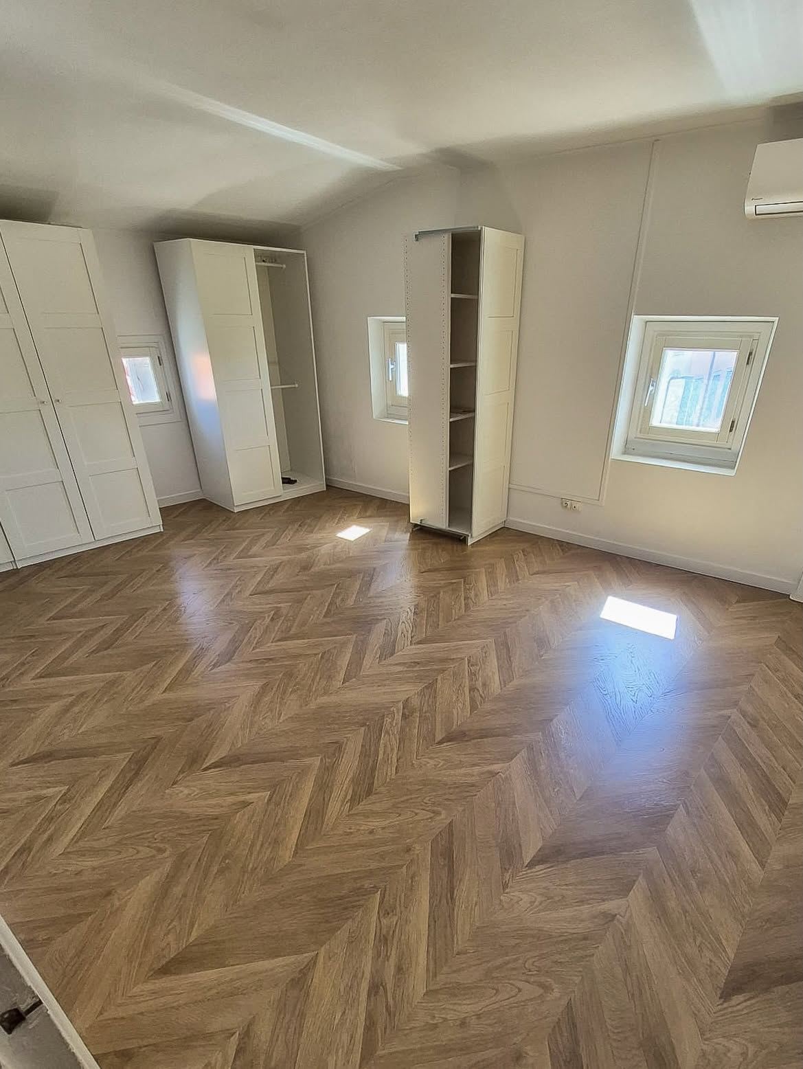 Pièce claire avec placards intégrés et parquet à chevrons posé jusque sous les portes