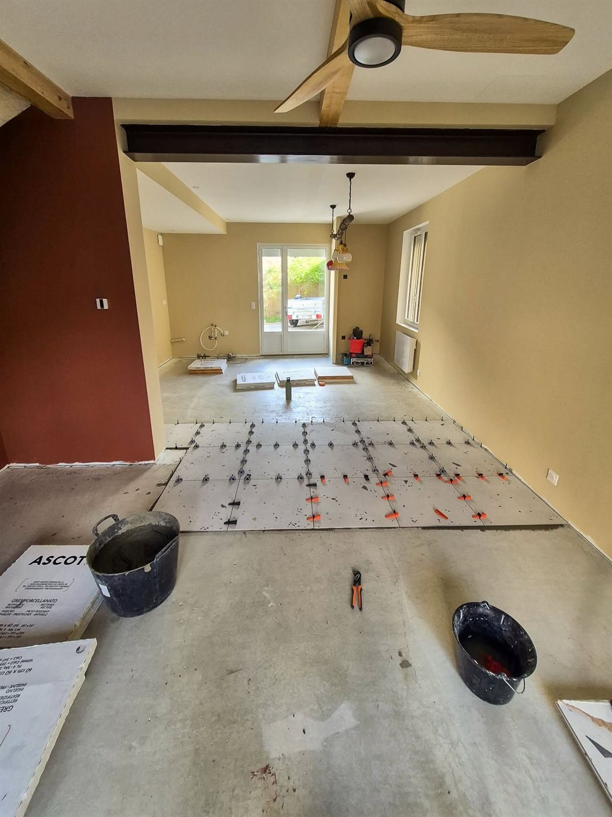 Pose d'un carrelage grand format 60 × 60 dans un séjour : premières dalles calées par des croisillons autonivelants sur la chape